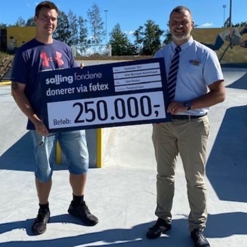 lokal donation Randers ildsjeald og varehuschef med skilt i solskin