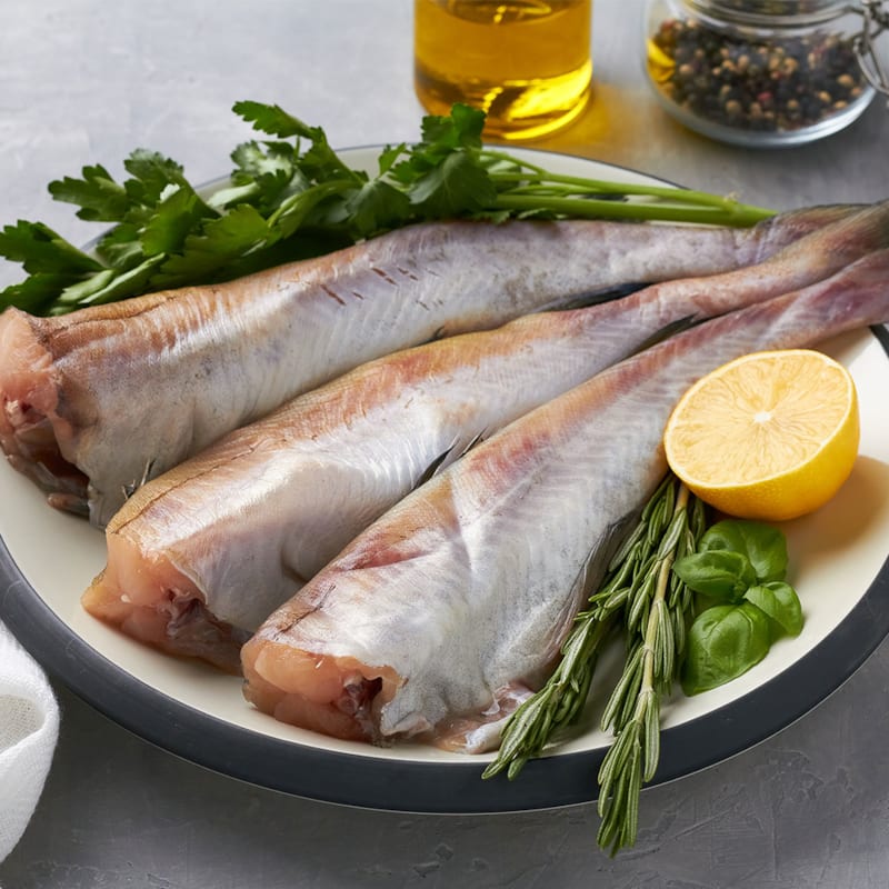 Tre friske alaska sej på tallerken med krydderurter og citron