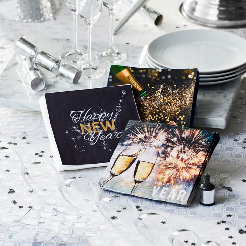 Nytårsservietter med tekst og champagneglas på bord med hvid du og sølv pynt.