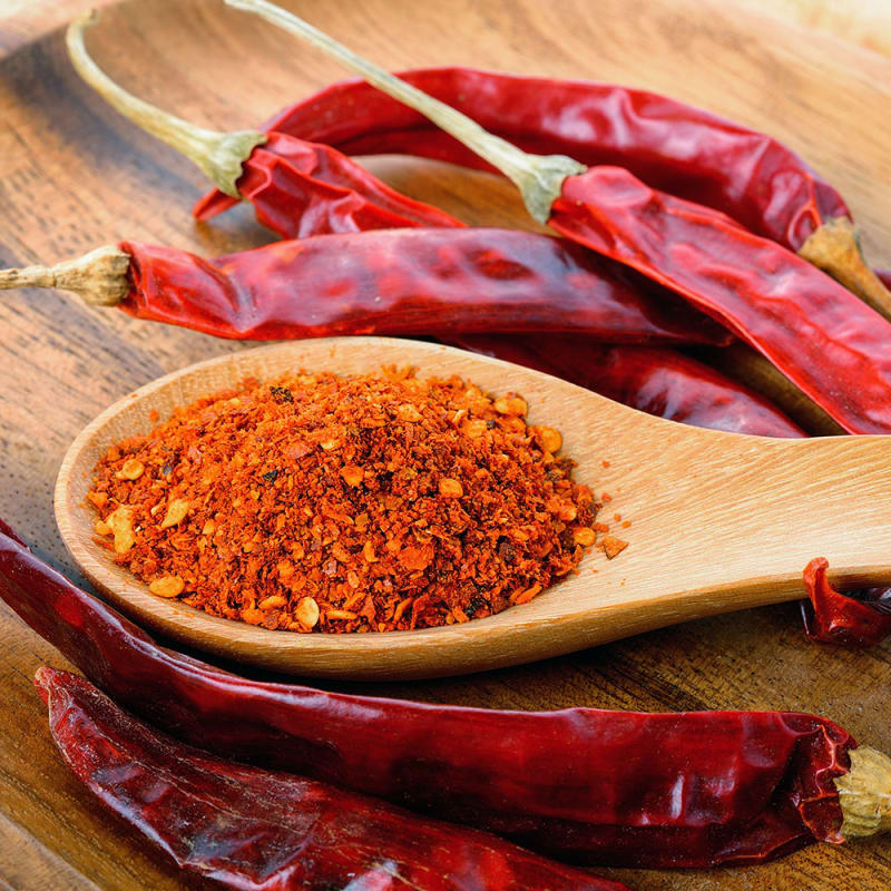 Cayennepeber på træske med tørret cayennepeber i baggrunden. 