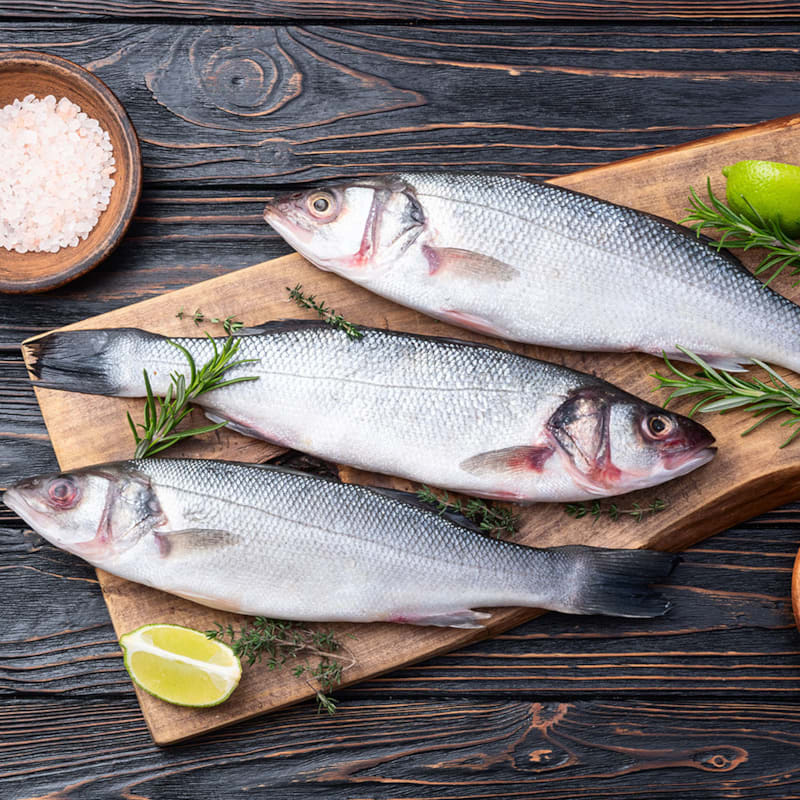 Tre friske havbars fisk på skærebræt med citron