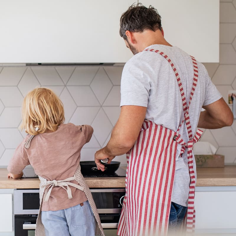 Et barn og en voksen står sammen i køkkenet og laver mad ved komfuret 