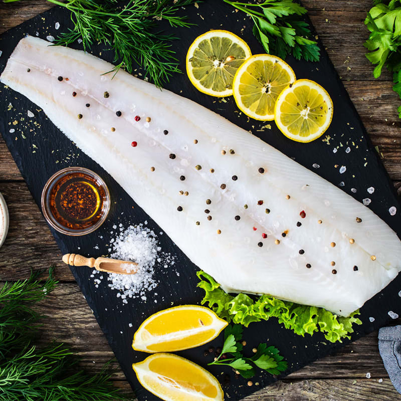 Rå hellefisk på skærebræt med citronskiver