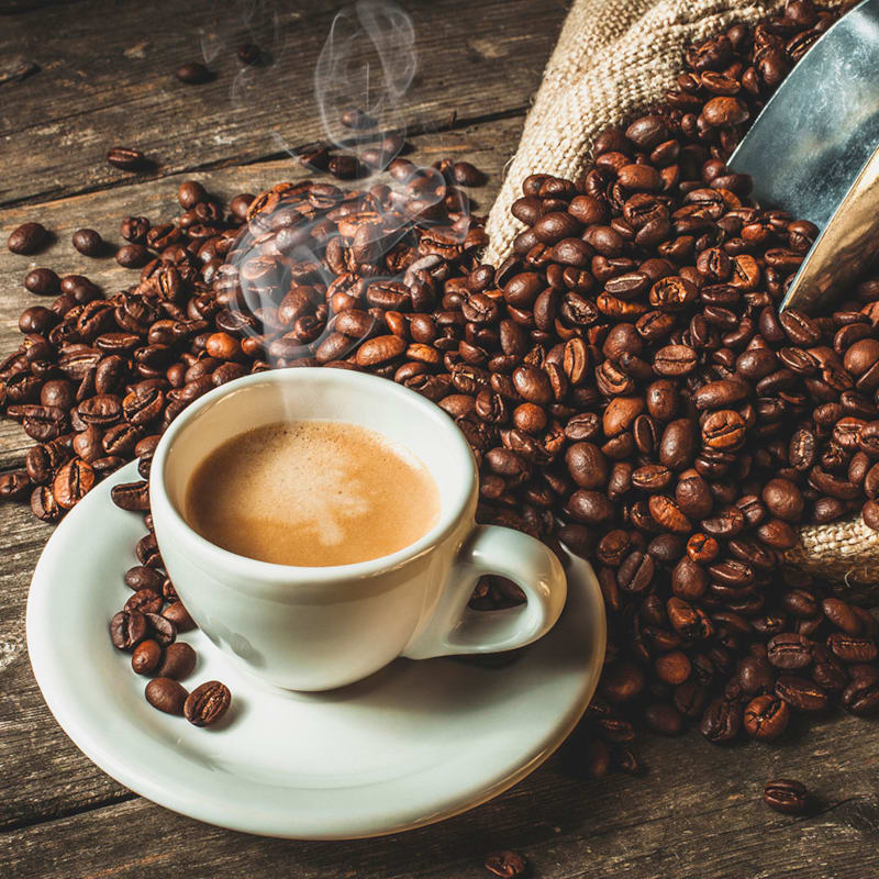 Varm kop kaffe og kaffebønner på bord.